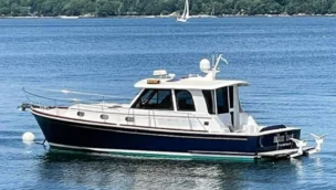 Profile view of a Grand Banks 39 Eastbay SX powerboat underway on calm blue water, highlighting its classic dark blue hull, white enclosed salon superstructure, and traditional Downeast design.