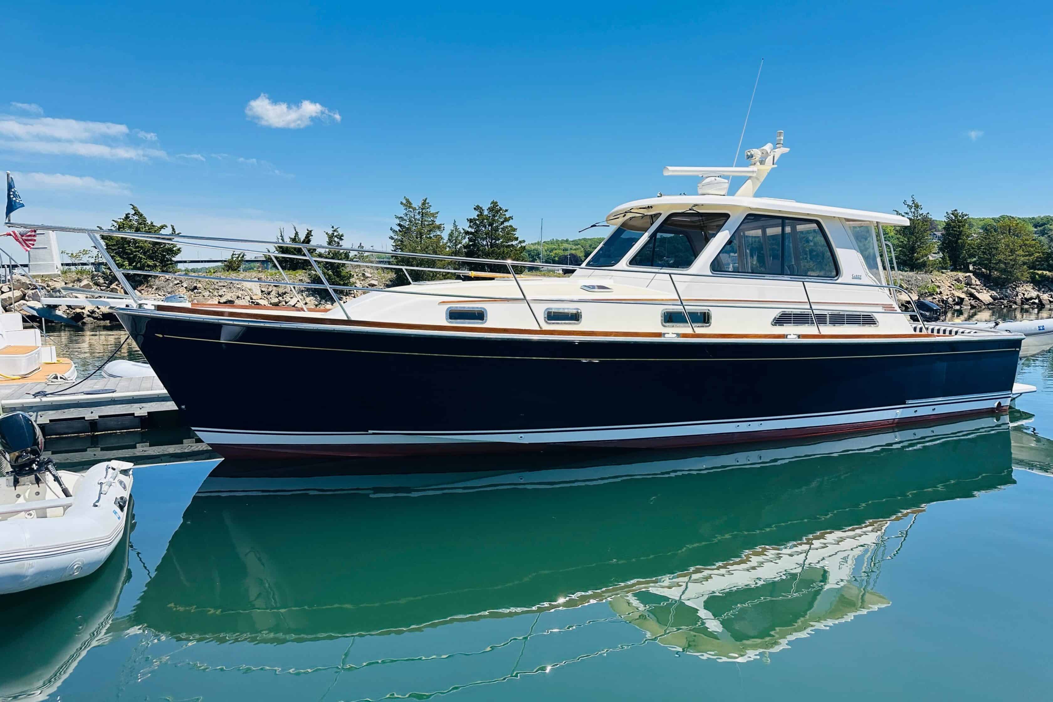 2006 Sabre 38 Hard Top Express yacht Piacere with an Awlgrip flag blue hull docked at a marina, reflecting in calm green water under a blue sky.