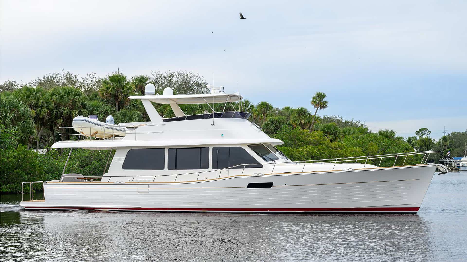 Side profile of the 2020 Grand Banks GB60 yacht SOUTHERLY cruising past a green shoreline