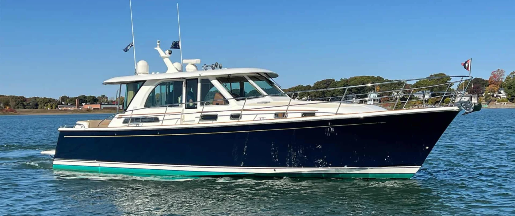A 2018 Sabre 45 Salon Express Downeast-style yacht with a midnight blue hull and white hardtop cruising on calm blue water on a sunny day.