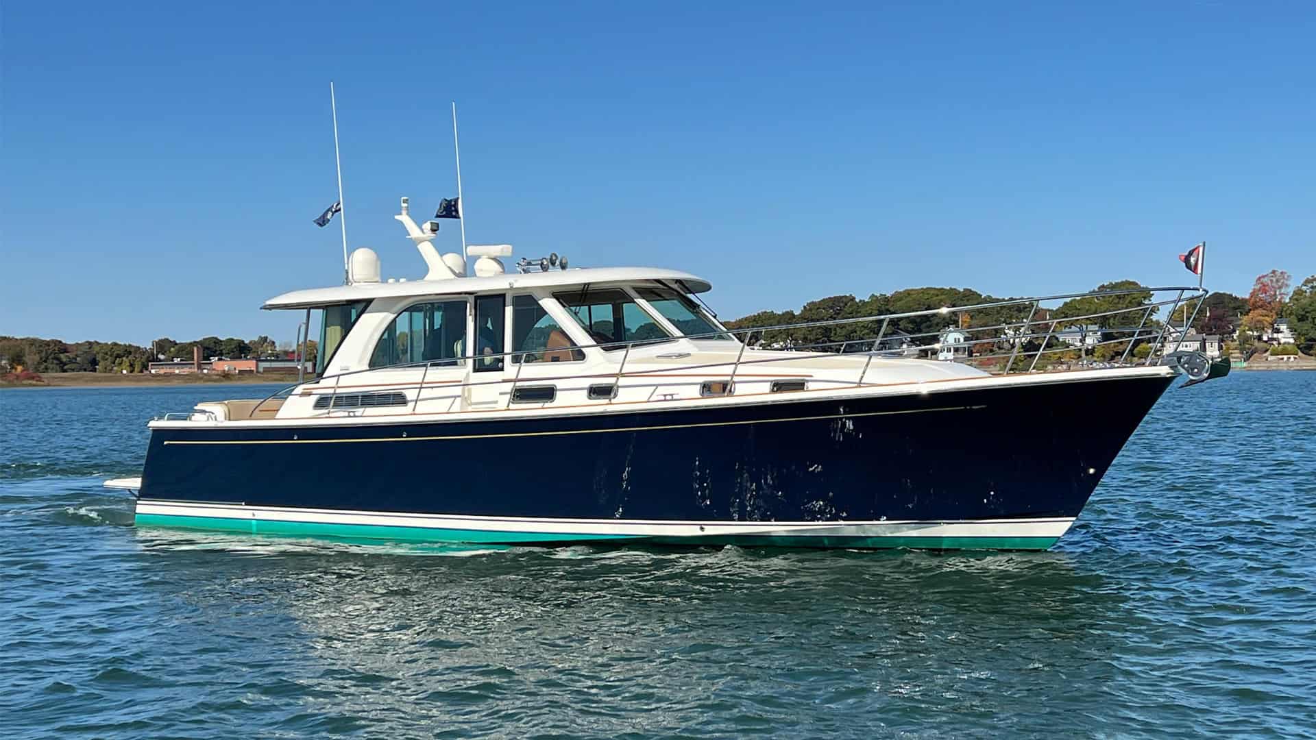 A 2018 Sabre 45 Salon Express Downeast-style yacht with a midnight blue hull and white hardtop cruising on calm blue water on a sunny day.