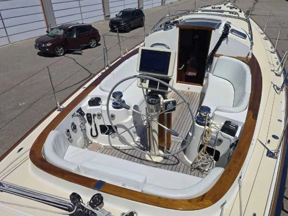 Cockpit of the Alerion 41 racer/cruiser looking forward, showing the large wheel helm, navigation plotter, and white cushions.