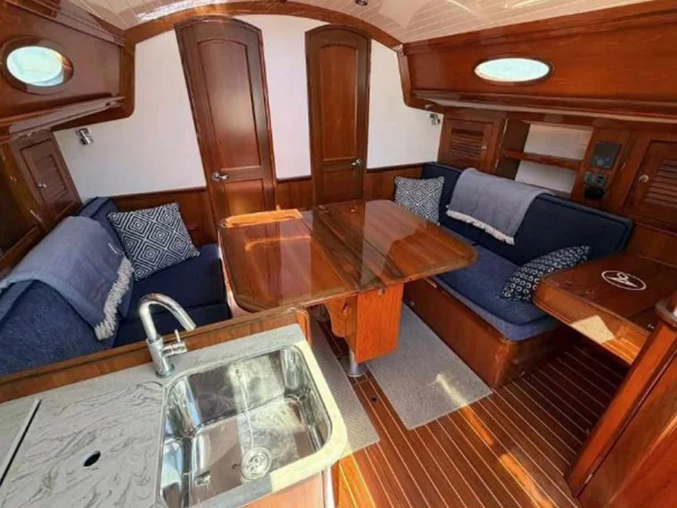 Main salon of the Alerion 41 sailboat "Sudan," showing the folding teak dining table, blue settees, and foreground galley sink.