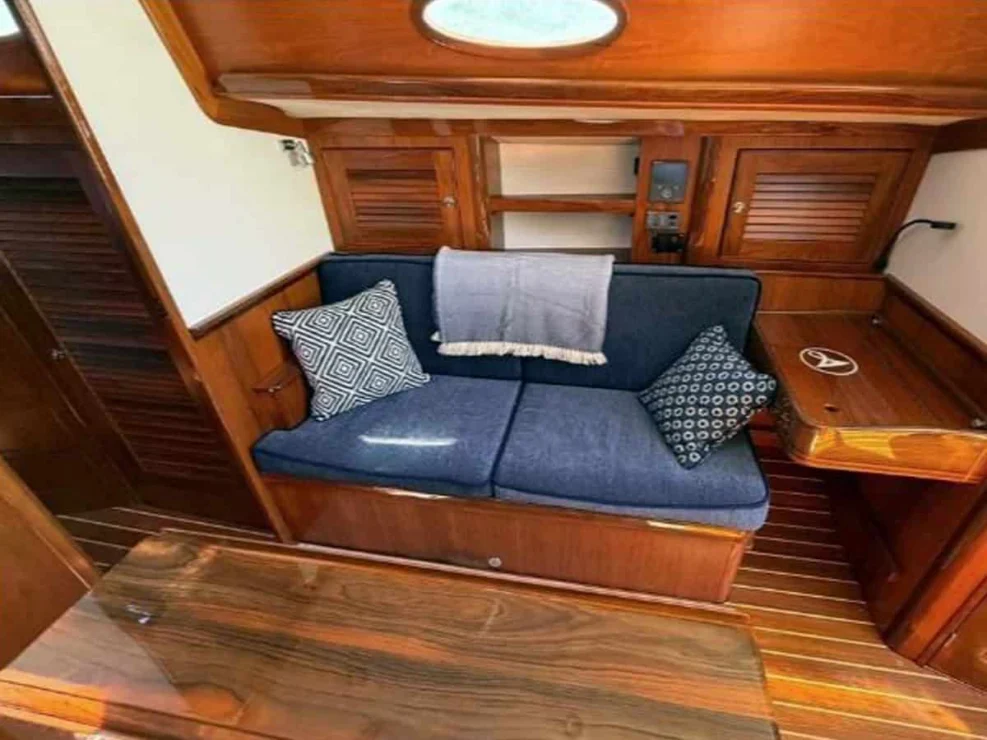Starboard settee in the Alerion 41 main cabin with blue velvet cushions, custom throw pillows, and varnished cherry wood cabinetry.