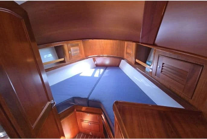 Brightly lit forward V-berth stateroom on the Alerion 41 cruiser, showcasing white hull ceilings and built-in cherry wood dressers.