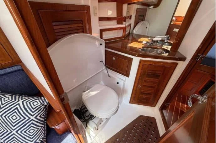Interior view of the Alerion 41 head compartment, showing the marine toilet with a folding privacy shroud, teak grating, and vanity sink.